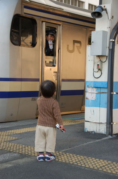 お父さんに連れられてかわいい男の子が電車を見に来ていました。車掌さんが手を振りながら列車は出発して行きました。